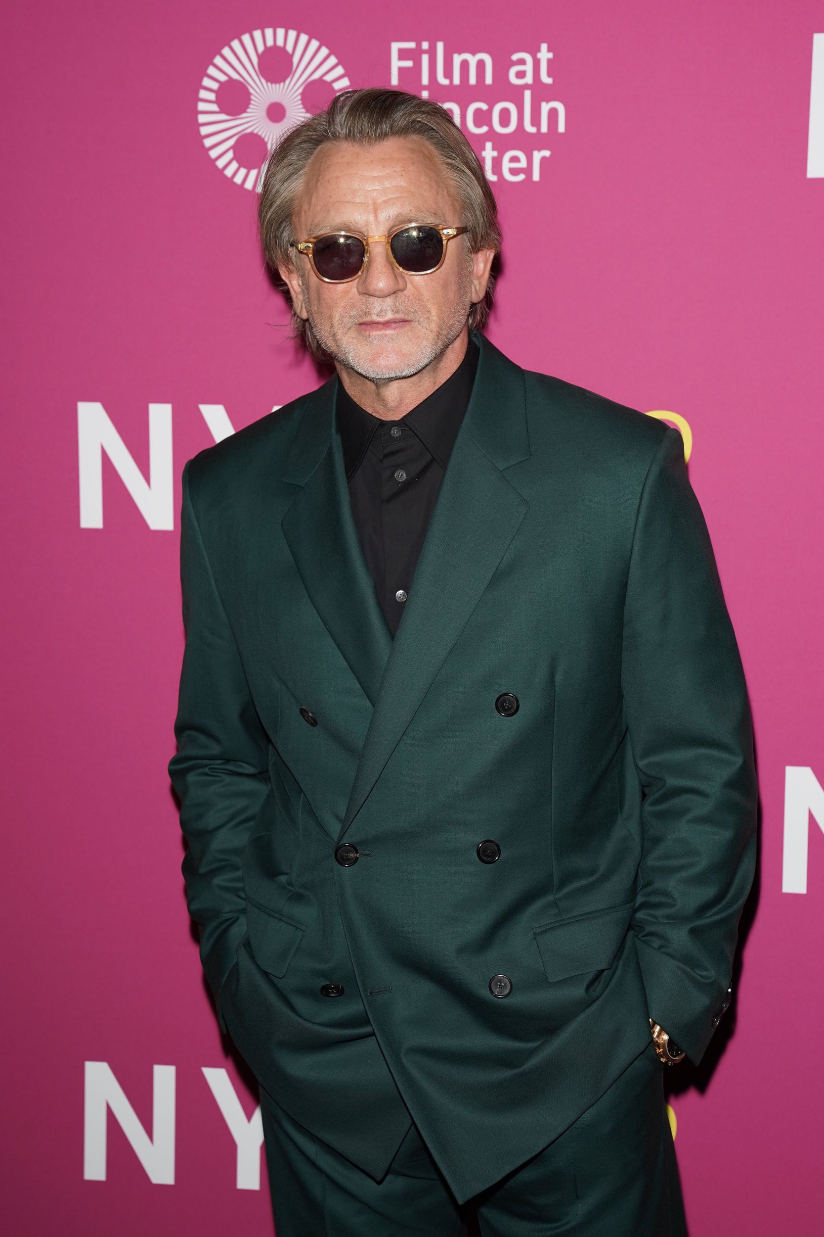Daniel Craig poses in square sunglasses and a dark green suit at the New York Film Festival